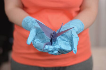 Origami paper crane in hand with rubber glovesの写真素材