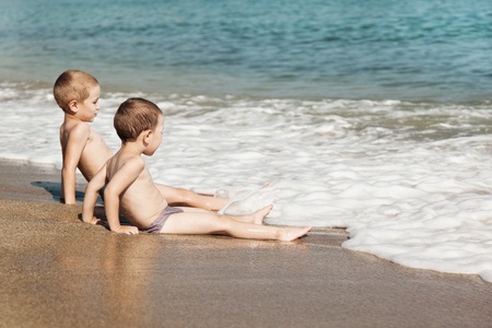 Summer vacations - two little child boy brothers playing on blue sea sand beachの写真素材