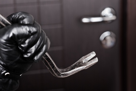 Crime scene - criminal thief or burglar hand in gloves holding metal crowbar break opening home door lockの写真素材