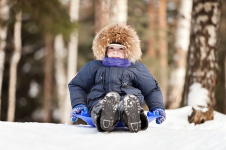 Little smiling child boy sled tobogganing on winter snow hillの写真素材