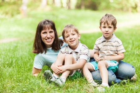 Beauty smiling mother and little sons walking outdoor on green grass fieldの写真素材