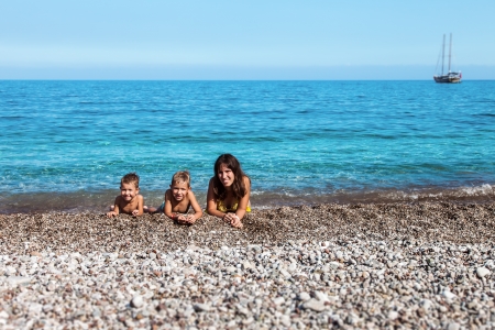 Summer vacations - happy mother with two little smiling child boy brothers playing on blue sea sand beachの写真素材