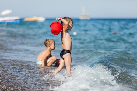 Summer vacations - two little child boy brothers playing on blue sea sand beachの写真素材