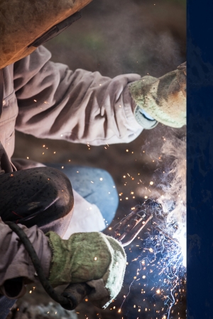 Heavy industry welder worker in protective mask hand holding arc welding torch working on metal constructionの写真素材