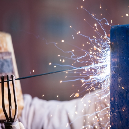 Heavy industry welder worker in protective mask hand holding arc welding torch working on metal constructionの写真素材