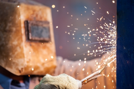 Heavy industry welder worker in protective mask hand holding arc welding torch working on metal...