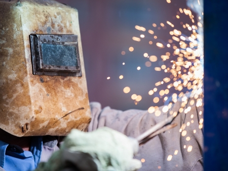 Heavy industry welder worker in protective mask hand holding arc welding torch working on metal constructionの写真素材