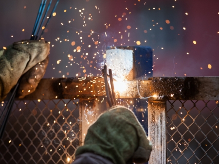 Heavy industry welder worker in protective mask hand holding arc welding torch working on metal...