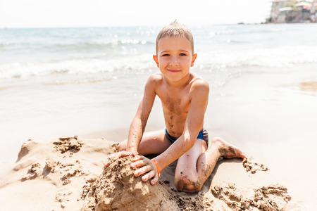 Summer vacations - little smiling child boy playing on blue sea sand beachの写真素材