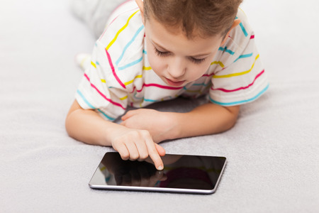 Little smiling child boy playing games or surfing internet on digital tablet computerの写真素材