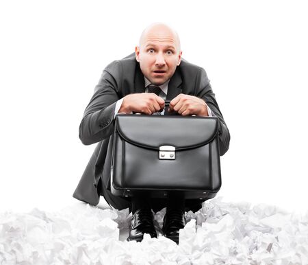 Business problems and failure at work concept - unhappy scared or terrified businessman in depression hand holding briefcase sitting down floor on crumpled torn paper document heap white isolatedの写真素材