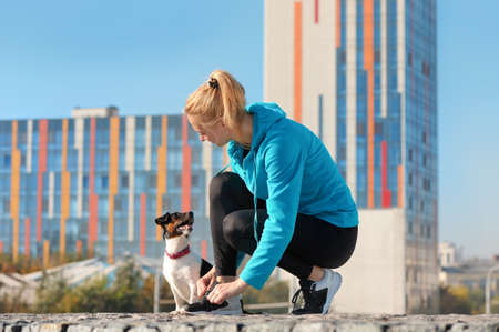 Sporty woman tying sneakers laces looking at her dog