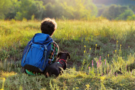 View from back of a boy with his dog sitting on the hillの写真素材