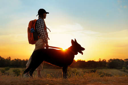 Full length of a woman with a dog against sundownの写真素材