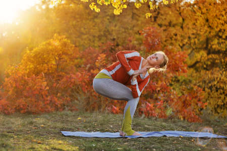 Sportive young woman practicing revolving chair yoga pose in the autumn forestの写真素材