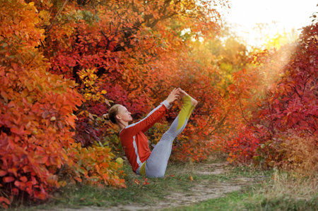 Woman practicing boat yoga pose against autumn treesの写真素材