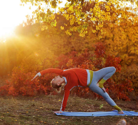 Yoga girl practicing side plank position at the sundown autumn parkの写真素材
