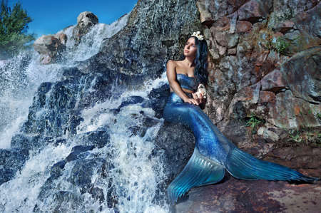 Beautiful mermaid sitting at the waterfall looking to the sideの写真素材