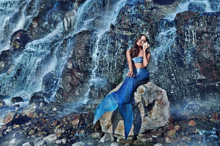 Mermaid against waterfall sitting on the rock listening to the shellの写真素材