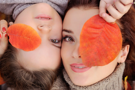 Close-up face portrait of mother and daughter with leaves in front of eyeの写真素材