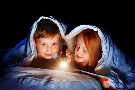 Brother and sister reading the book under the blanket using flashlightの写真素材