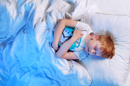 Top view of a boy in bed hugging blue clockの写真素材