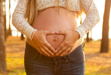 young couple holding pregnant belly in the sunset
