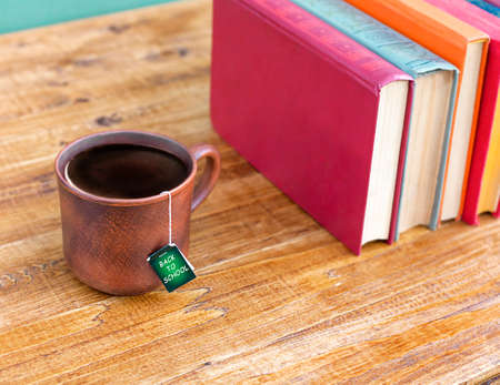 mug with tea and stack of books on wooden tableの写真素材