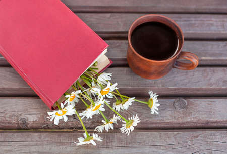 a book with daisies and a mug of tea on a wooden surface. View from aboveの写真素材