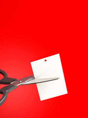 white tag clamped in scissors close-up on a red backgroundの写真素材