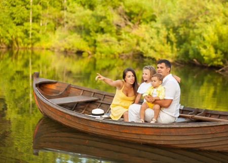 Happy family of four sitting in a boat on the lake and looking awayの写真素材