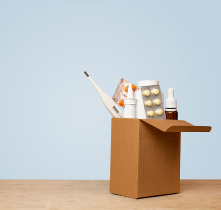 Box with medicines and a thermometer on a wooden table against a blue backgroundの写真素材