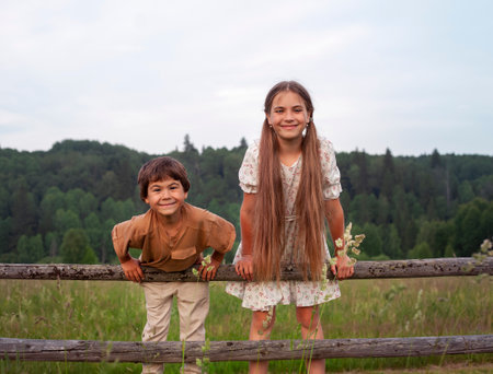 Two children, boy and girl, standing on a wooden fence in the villageの写真素材