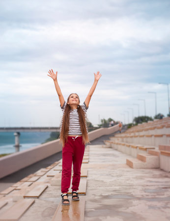 a little girl stands with her hands up on the embankment on a summer dayの写真素材