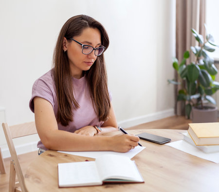 Serious girl with glasses writes in a notepad at homeの写真素材