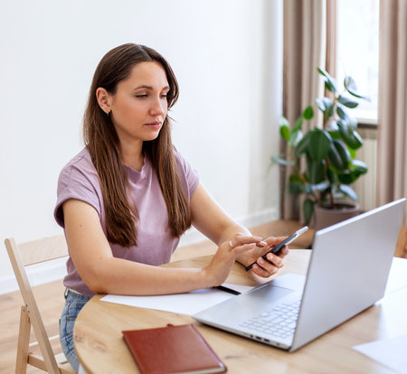 Portrait of a young woman using mobile phone and laptop at homeの写真素材