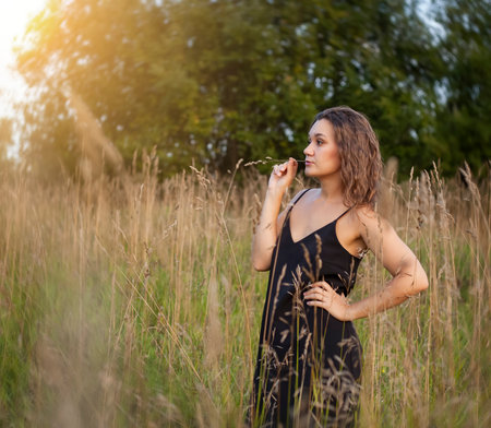 Beautiful young woman in a black dress in the field at sunsetの写真素材
