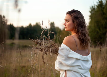 Beautiful young girl in a white dress in the field at sunsetの写真素材