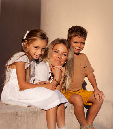 Portrait of a beautiful mother with her two children sitting on the stairsの写真素材