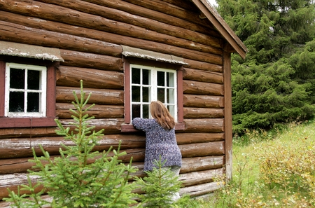 Woman outside an old cottage looking in through a windowの写真素材