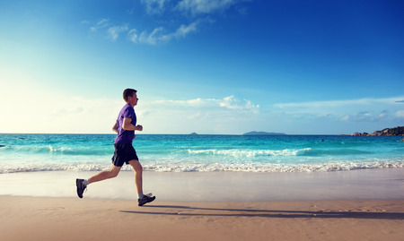 Man running on tropical beach at sunsetの写真素材