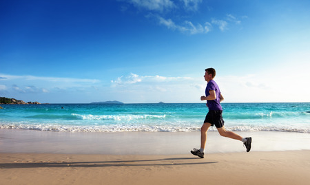 Man running on tropical beach at sunsetの写真素材