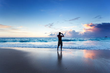 young man on the beach take photo on mobile phoneの写真素材