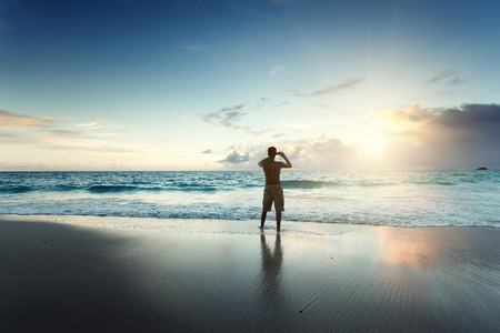 young man on the beach take photo on mobile phoneの写真素材