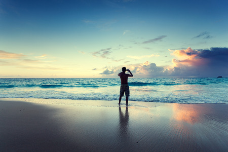 young man on the beach take photo on mobile phoneの写真素材