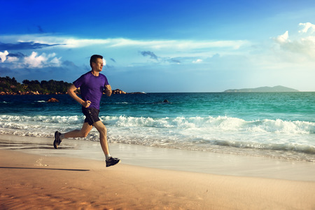 Man running on tropical beach at sunsetの写真素材