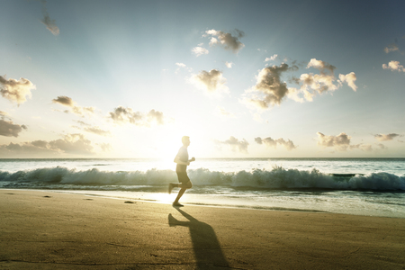 Man running on tropical beach at sunsetの写真素材