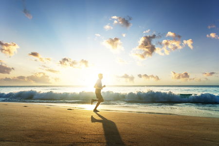 Man running on tropical beach at sunsetの写真素材