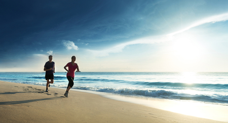 Man and women running on tropical beach at sunsetの写真素材
