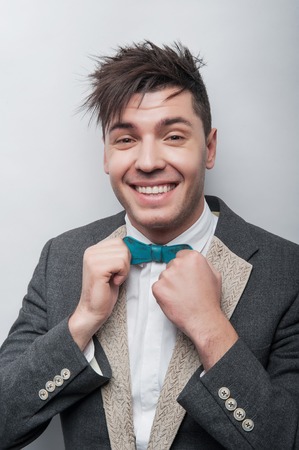 Hey tere . hipster wearing suit and touching his bow tie. while standing against grey background